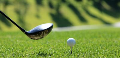 Glänzender Golfschläger neben einem zum Abschlag bereitliegenden Golfball auf grünem Rasen