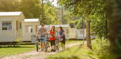 Drei abgestiegene Radfahrer laufen einen sonnigen Campingplatz entlang